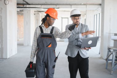 Bina teftişi sırasında mimarla proje detaylarını tartışırken dizüstü bilgisayarı tutan ve bir şeyi işaret eden mimar