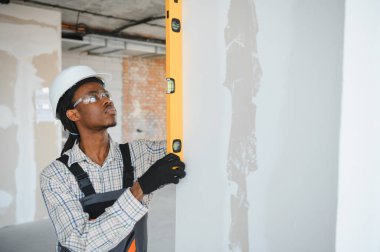 Genç Afrikalı Amerikalı inşaatçı inşaat sırasında tam olarak dikey hizalama sağlamak için ruh seviyesini kullanıyor.