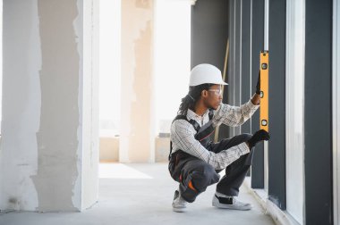 Genç Afro-Amerikan inşaat işçisi inşaat halindeki binaya pencere çerçeveleri yerleştirirken ruh seviyesini kullanıyor