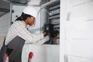 Güvenlik gözlüğü takan elektrikçi inşaat halindeki bir binada havalandırma kontrol paneli üzerinde çalışıyor.