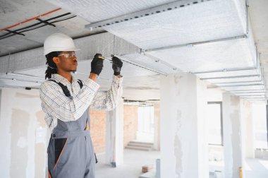 Afrikalı Amerikalı inşaat işçisi inşaat sahasına havalandırma sistemi kuruyor, tavanda tornavida kullanıyor.