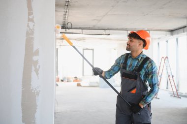 İnşaat halindeki bir binada teleskopik saplı fırçayla duvarları boyayan bir Arap müteahhit.