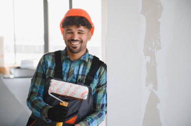 Bir inşaat sahasında boya silindiri tutarken gülümseyen genç Arap mühendis, iç yenileme çalışmaları için coşku gösteriyordu.