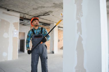 İnşaat işçisi, inşaat alanındaki yüksek duvarları ve tavanları boyamak için teleskopik boya silindiri kullanıyor.