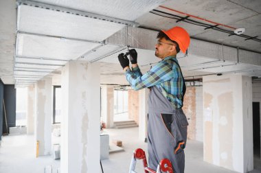 Elektrikçi bitmemiş bir binanın merdiveninde düzgün kurulum ve bakım sağlarken havalandırma sistemi üzerinde çalışıyor.