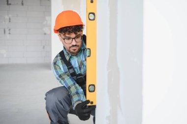 Arap inşaatçı, yoğun bir inşaat sahasında duvar yüksekliğini ruh seviyesiyle ölçerek projede hassasiyet ve kalite sağlıyor.