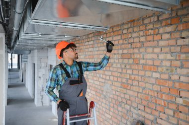 Arap hvac uzmanı, yoğun bir inşaat sahasında çalışırken hava kanalının vidalarını sıkıyor ve düzgün kurulumunu sağlıyor.