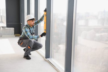 Arap inşaatçı inşaat halindeki modern bir binaya pencereler yerleştirirken ruhsal düzeyini kullanır, hassas hizalama ve kaliteli işçilik sağlar