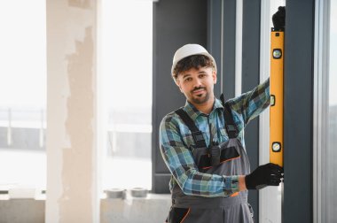 Bir ev yenileme projesi üzerinde çalışırken bir pencere çerçevesinin ruh seviyesiyle dikey hizasını kontrol eden Arap inşaatçı