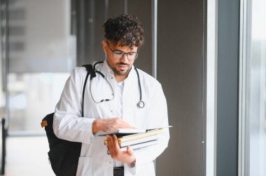 Odaklanmış Arap tıp öğrencisi ders kitapları okuyor, parlak bir üniversite koridorunda sınavlara hazırlanıyor.