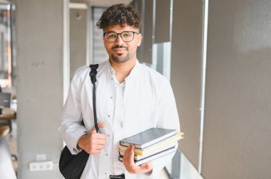 Kitap ve sırt çantası taşıyan kendinden emin bir tıp öğrencisi, parlak bir üniversite koridorunda yürüyor, akademik başarının ruhunu somutlaştırıyor.