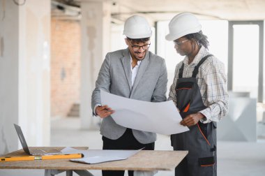 İnşaat alanının planlarını inceleyen mimar ve müteahhit inşaat planlarını tartışıyor ve proje ilerlemesini tartışıyordu.