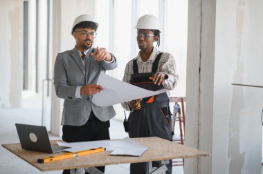 Mimar ve inşaatçı inşaat toplantılarında planlarını gözden geçirir, bina planlarını ve proje ilerlemesini tartışır.