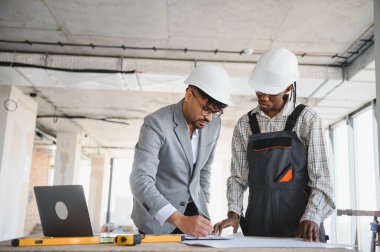 İnşaat halindeki bir binanın planlarını gözden geçiren mimar ve inşaat işçisi.