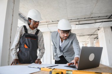 Mimar ve müteahhit, inşaat halindeyken dizüstü bilgisayarın planlarını tartışıyorlar.