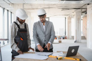Mimar ve müteahhit, inşaat halindeki bir binada dizüstü bilgisayarla ve ruhsal seviyeyle masanın planlarını tartışıyorlar.
