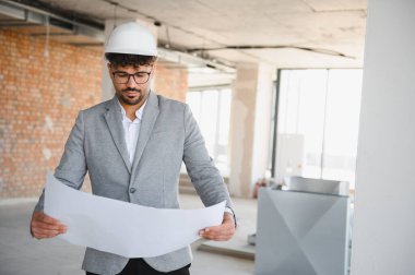 Bir inşaat sahasının ayrıntılı planlarını inceleyen Arap mimar, sıkı bir şapka ve özel dikim takım elbise giyerek proje geliştirmeye odaklandı.