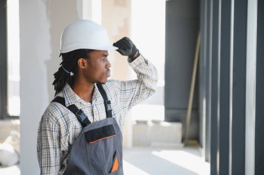 Genç Afro-Amerikan inşaat işçisi inşaat alanını incelerken şapkasını düzeltiyor.