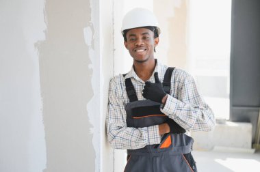 Genç Afro-Amerikan inşaat işçisi inşaat halindeki bir binada dikilirken gülümsüyor ve el sallıyor.