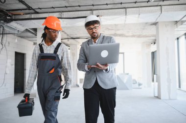 İnşaat halindeki tamamlanmamış bir binada yürürken dizüstü bilgisayarı sunan mimar, proje detayları ve planlarını tartışıyor