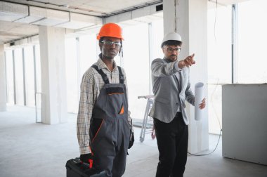 İnşaat sırasında alet çantası taşıyan inşaatçıya talimatları gösteren planlar tutan mimar