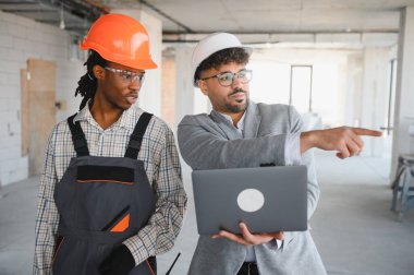İnşaat alanındaki inşaatçıyla proje detaylarını tartışırken dizüstü bilgisayar tutan ve bir şeyi işaret eden mimar