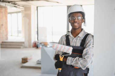 Elinde boya silindiri tutan, inşaat halindeki bir binada duran gülümseyen Afrikalı Amerikalı bir inşaat işçisinin portresi.