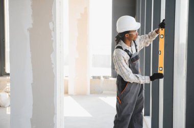 Afro-Amerikalı inşaatçı inşaat halindeki bir binanın pencere kurulumunda çalışırken ruh seviyesini kullanıyor