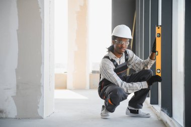 Genç Afro-Amerikalı inşaatçı, bir inşaat sahasında ruhsal seviye ile pencere seviyesini kontrol ediyor, hassasiyet ve hizalama sağlıyor.