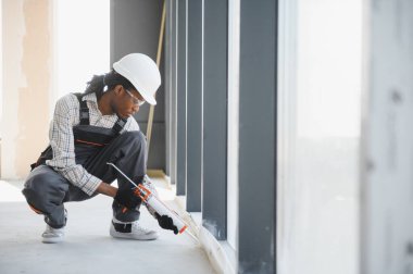Kaliteli inşaat işçisi pencere çerçevesine dolgu macunu sürüyor, inşaat halindeki bir binaya hava geçirmez ve hava geçirmez kurulum sağlıyor
