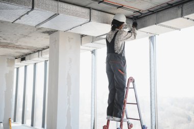 Afrika kökenli Amerikalı inşaat işçisi hareketli bir şantiyeye havalandırma boruları yerleştiriyor ve verimli bir HVC sistemi kurmaya odaklanıyor.