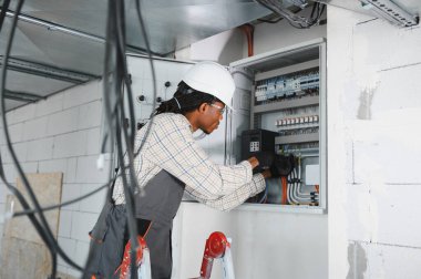 Merdivendeki elektrikçi inşaat halindeki bir binanın havalandırma kontrol paneli üzerinde çalışıyor.