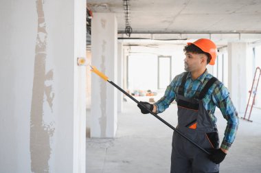 İnşaat işçisi, inşaat halindeki bir binanın duvarlarını etkili bir şekilde boyamak için teleskopik boya silindiri kullanıyor.