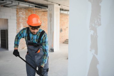 Turuncu bir miğfer ve üniforma giyerek inşaat alanını süpüren Arap müteahhit yoğun bir çalışma ortamında temizlik sağlıyor.