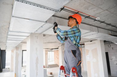 Arap mühendis bir inşaat sahasına havalandırma ya da havalandırma sistemi kuruyor, merdiven üzerinde çalışıyor ve güvenlik ekipmanı takıyor.