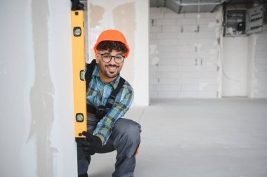 Bir inşaat sahasında gülümseyen ve ruh seviyesini kullanan Arap mühendis, proje inşaatı için kesin ölçümler sağlıyor