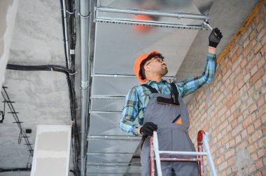 Hvac teknisyeni inşaat halindeki bir binaya havalandırma sistemi kuran bir merdiven üzerinde çalışıyor.