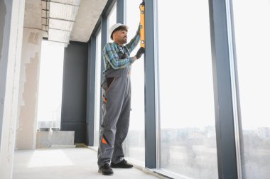 Bir pencere çerçevesinin ruh seviyesiyle hizalanmasını kontrol eden Arap inşaatçı, şantiyedeki inşaat sürecinde doğruluğu garanti ediyor