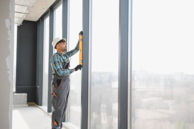 Arap inşaat işçisi, pencere çerçevesini ruh seviyesiyle aynı hizaya getirerek modern bina inşaatında hassas bir yerleşim sağlıyor.