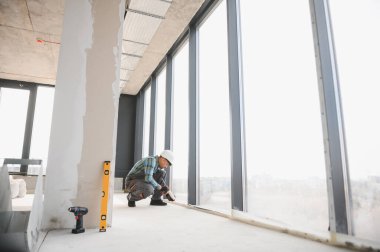 Modern bir ofis binasına kablosuz tornavida ve ruhsal seviye kullanarak pencere kuran inşaat işçisi