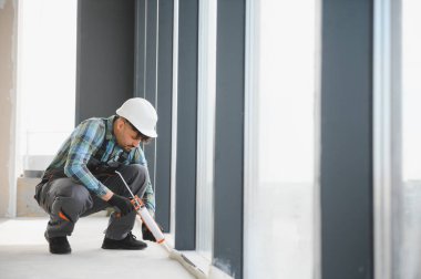 İnşaat işçisi, hareketli bir şantiyedeki geniş bir pencere çerçevesine silikon dolgu maddesi sürerek su geçirmez ve yalıtımlı bir kaplama sağlıyor.