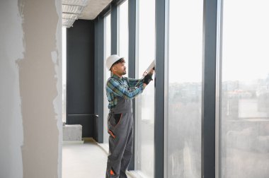 Arap inşaat işçisi inşaat halindeki modern bir binanın pencere çerçevesine dolgu macunu sürüyor.