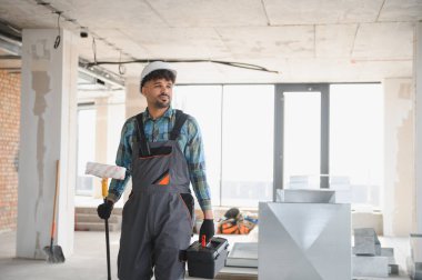 İnşaat halindeki bir binanın içinde yürüyen bir Arap mühendis boya silindiri ve alet çantası taşıyor.