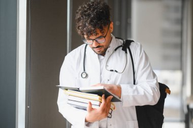 Bir üniversite koridorunda ders kitapları okuyan Arap tıp öğrencisi, çalışmalara dalmış ve sağlık sektöründe bir geleceğe hazırlanıyor.