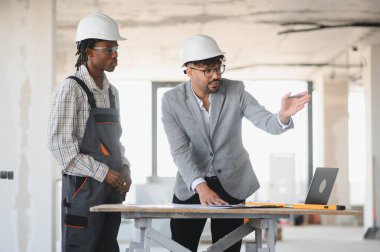 İnşaat planını açıklayan mimar, site ziyareti sırasında dizüstü bilgisayar ve planlar kullanarak inşa edecek.