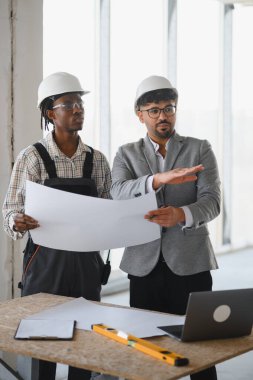 İnşaat alanının planlarını inceleyen mimar ve inşaatçı, proje planları ve ilerlemesini tartışıyor