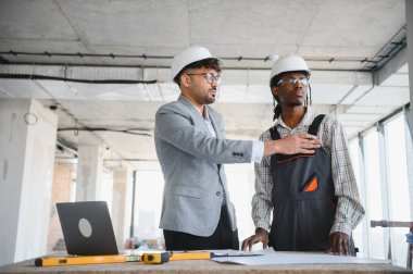 İnşaat sahasındaki bir toplantı sırasında bir mimarın planlarını gösteren, bina planlarını tartışan ve proje ilerlemesini tartışan mimar