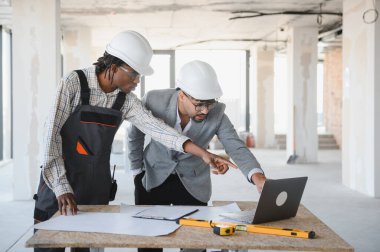 Tamamlanmamış bir binada inşaat planlarını tartışan mimar ve müteahhit takım çalışması ve proje yönetimi