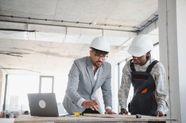 Mimar ve müteahhit başlık takıyor, planları inceliyor ve hareketli bir inşaat sahasının planları üzerinde işbirliği yapıyor, proje başarısını güvence altına alıyor.