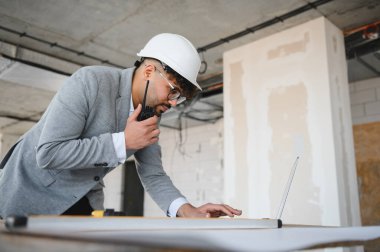 Arap mimar inşaat sahasında çalışırken telsiz ve dizüstü bilgisayar kullanıyor.